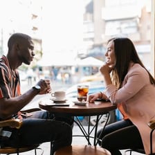 Two people exchange playful expressions while talking in a café.