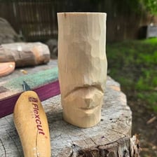 A person whittling a piece of wood with a knife
