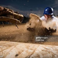 A baseball runner sliding toward home plate as the catcher awaits the throw.