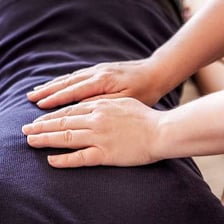 A reiki practitioner holding their hands over a seated recipient.