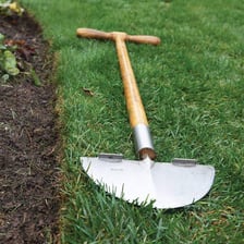 A lawn edger being used to define the border of a grassy lawn.