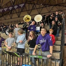 A school pep band plays brass instruments in the stands at a game.