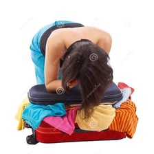 A person forcing clothing into an overstuffed suitcase.