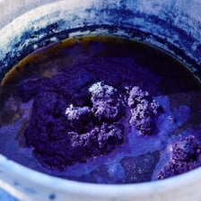 Blue indigo dye in a vat beside dyed textile
