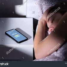 A smartphone alarm sounds beside a person sleeping in bed.
