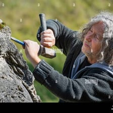 A sculptor shapes a block of stone with a chisel.