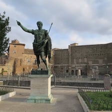 A statue of Julius Caesar stands in a Roman setting.