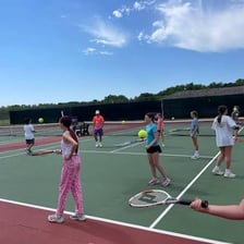 A tennis instructor giving a lesson to a student on a court.
