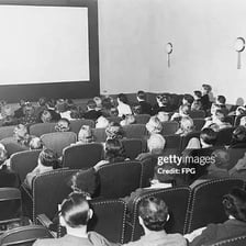A movie screen in a cinema with viewers seated in front of it.