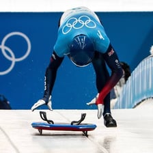 An athlete riding a skeleton sled headfirst down an icy track.