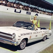 A pace car leading a group of race cars around a track.