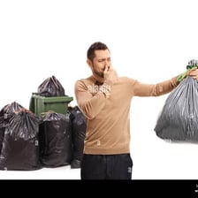 A person reacts to an unpleasant smell near a garbage bin.