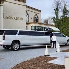A stretch limousine waiting for passengers with a chauffeur nearby.
