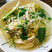 A bowl of pho served with a plate of fresh bean sprouts and herbs.