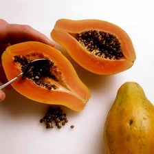 A halved papaya with its seeds being removed using a spoon.