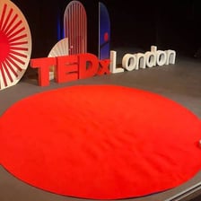 A speaker giving a TED Talk on a red circular stage.