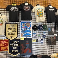 A concert merch table displays T-shirts and posters.