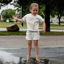 A toddler jumping in a rain puddle while wearing rain gear.