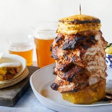Al pastor pork being shaved from a vertical spit onto tacos.