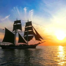A historic sailing vessel with a dark treated canvas sail.