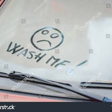 A dirty vehicle window bearing the words “Wash Me”