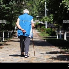 A person walks with a noticeable limp along a sidewalk.