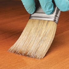 A brush applying transparent varnish to a wooden surface