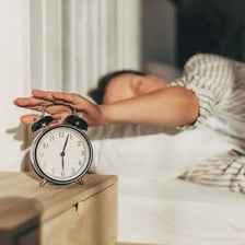 A person waking beside an alarm clock in the morning.