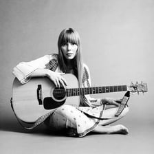 Joni Mitchell performing with a guitar.