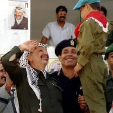 A historical photograph of Yasser Arafat at a Palestine Liberation Organization event