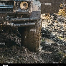 A vehicle tire caught in a deep muddy road rut.