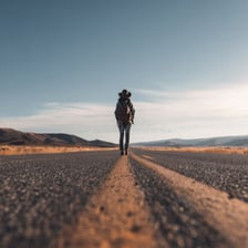A solitary traveler walking along an open, empty road.
