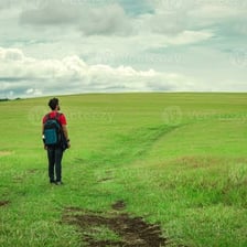 A person wandering through an open countryside landscape.