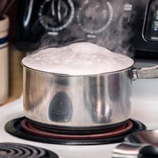 Water bubbling over the rim of a pot on a stove.