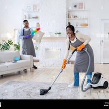 A person dusting furniture and vacuuming a floor.