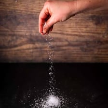 A hand adding only a small amount of salt to food.