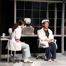 A theatre professional discussing a play script with performers and directors during rehearsal