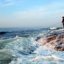 An angler casting a fishing line from a beach into the ocean surf.