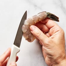 A cook removing the vein from the back of a peeled prawn.