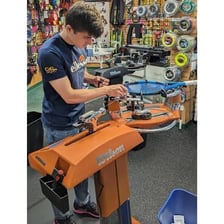 A technician fitting new strings into a tennis racket frame