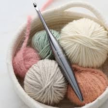 A metal crochet hook drawing a loop through yarn.