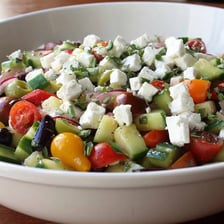 A Greek salad containing crumbled feta cheese, tomatoes, cucumber, and olives.