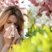 A person sneezing outdoors near flowering plants, illustrating an allergic reaction.
