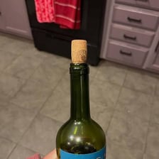 A wine bottle with its cork removed beside a wine glass.