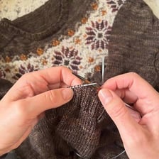 A person using knitting needles to make a sweater