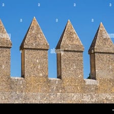 A stone castle wall with a crenellated battlement.