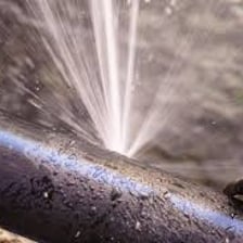 A ruptured pipe spraying water from a split opening.