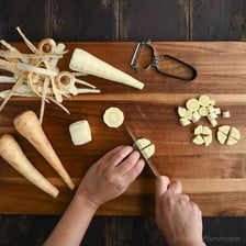 Hands cutting peeled parsnips into pieces on a cutting board