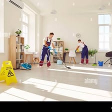 Person dusting furniture beside a vacuum cleaner.