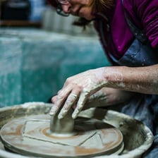 A ceramicist shaping a clay vessel on a pottery wheel.